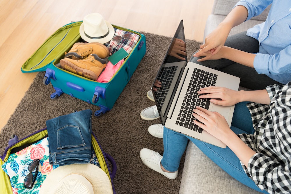 couple with laptop out looking online while sitting next to an open, packed suitcase