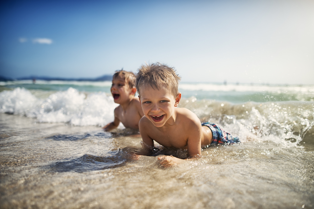 two little boys laying in waves on beach