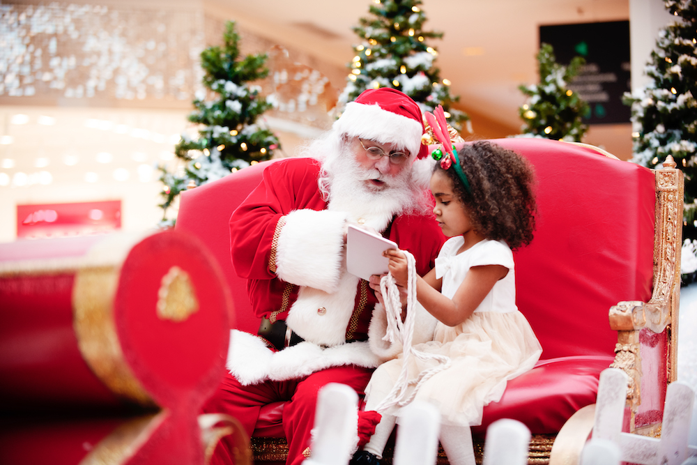 Santa Claus talks to a little girl who is showing him her Christmas list